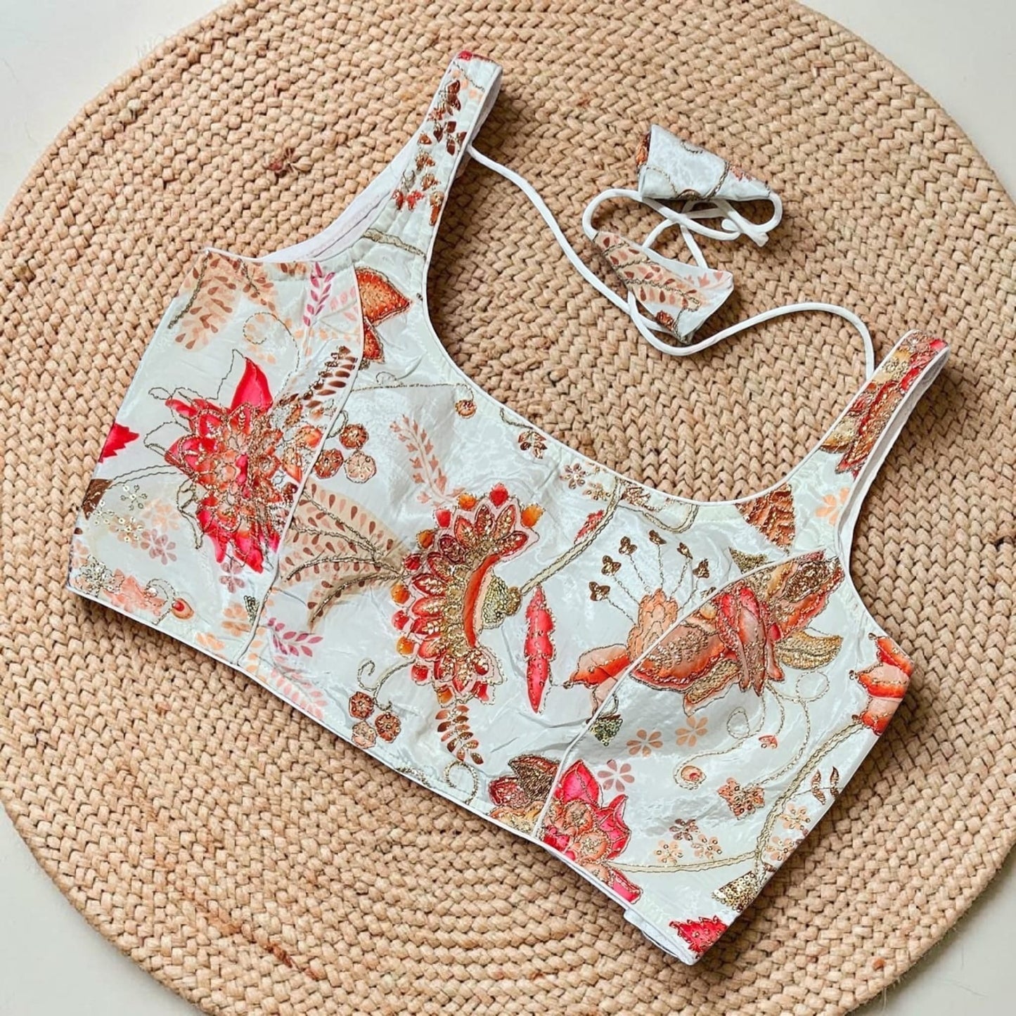 Manishaa's Boutique white sleeveless padded saree blouse with red and orange floral embroidery. Adjustable tie closure.